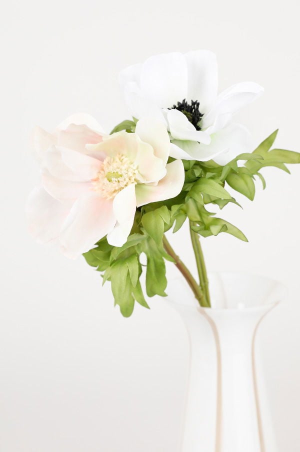 Vacker bukett med en rosa och en vit anemone i en elegant vit vas, omgiven av grönska.