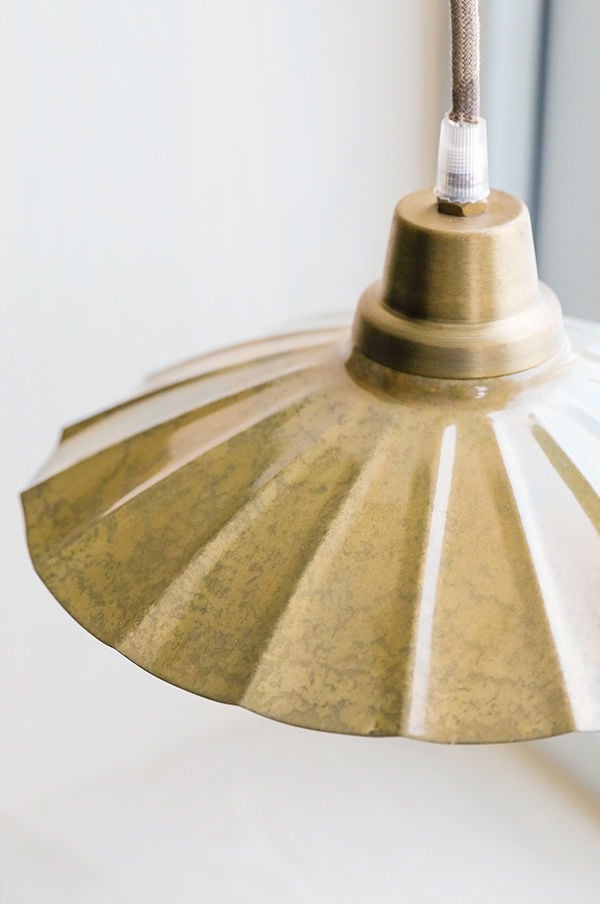Taklampa i metall med en vintage design och en gyllene yta, hängande från en textilkabel. Idealisk för att skapa en stilren och modern atmosfär i hemmet.