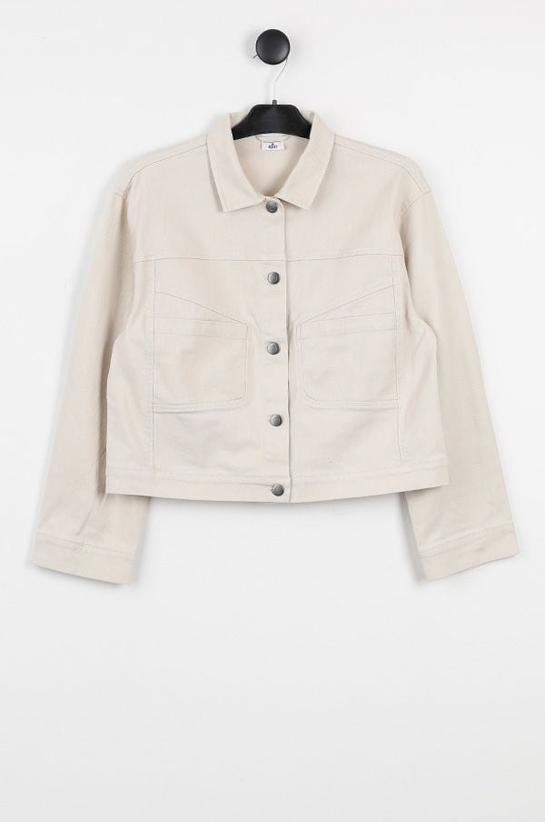 Beige kort jacka med knäppning, två framfickor och krage, hängande på en klädhängare. Perfekt för vår- och höstmode.