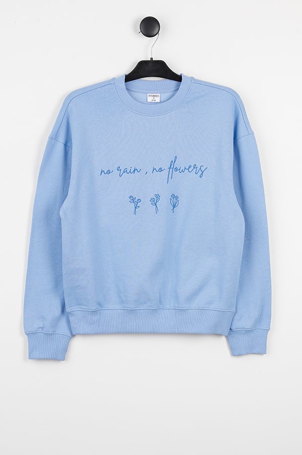 Ljusblå sweatshirt med broderad text "no rain, no flowers" och blommotiv, perfekt för avslappnade outfits och vårmode.
