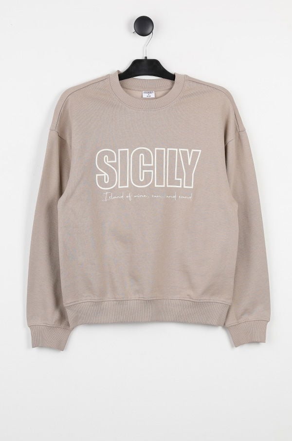Beige sweatshirt med texten "SICILY" och undertexten "Island of wine, sun and sand", hängande på en klädhängare mot vit bakgrund. Perfekt för avslappnade stilar.