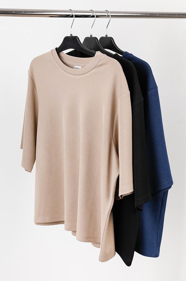 Tre t-shirts i olika färger hängande på en klädhängare, inklusive beige, svart och marinblå. Perfekta för avslappnad stil och vardagsbruk.