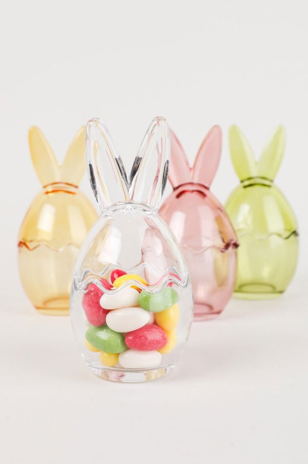 Färgglada påskägg i glas med godis inuti, omgivna av transparenta och pastellfärgade ägg. Perfekt dekoration för påskfirande.