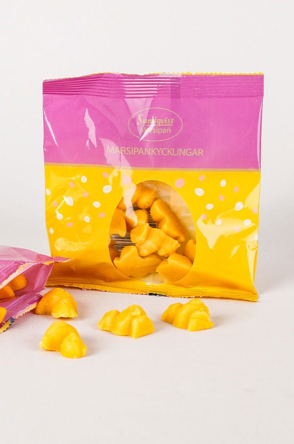 Förpackning med marsipankycklingar i gul och rosa design, med flera gula marsipankycklingar synliga både inuti och utanför förpackningen.