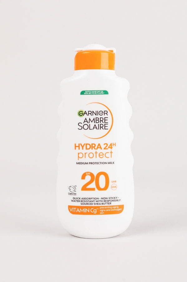 Flaska med Garnier Ambre Solaire Hydra 24H protect solskyddsmedel, SPF 20, för medel skydd. Snabbabsorberande och vattentålig formel med sheasmör och vitamin C, designad för att skydda huden mot solens skadliga strålar.