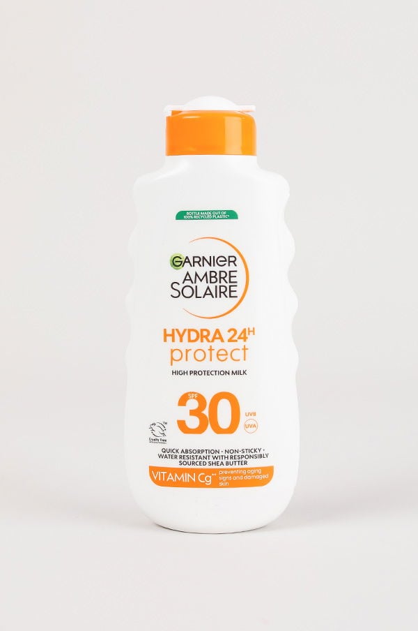 Flaska med Garnier Ambre Solaire Hydra 24H Protect solskyddsmjölk, SPF 30, som erbjuder hög skyddsnivå mot UVA- och UVB-strålar. Produkten är snabbabsorberande, icke-klibbig och vattenresistent, berikad med vitamin Cg och sheasmör för att förebygga ålderstecken och skador på huden.
