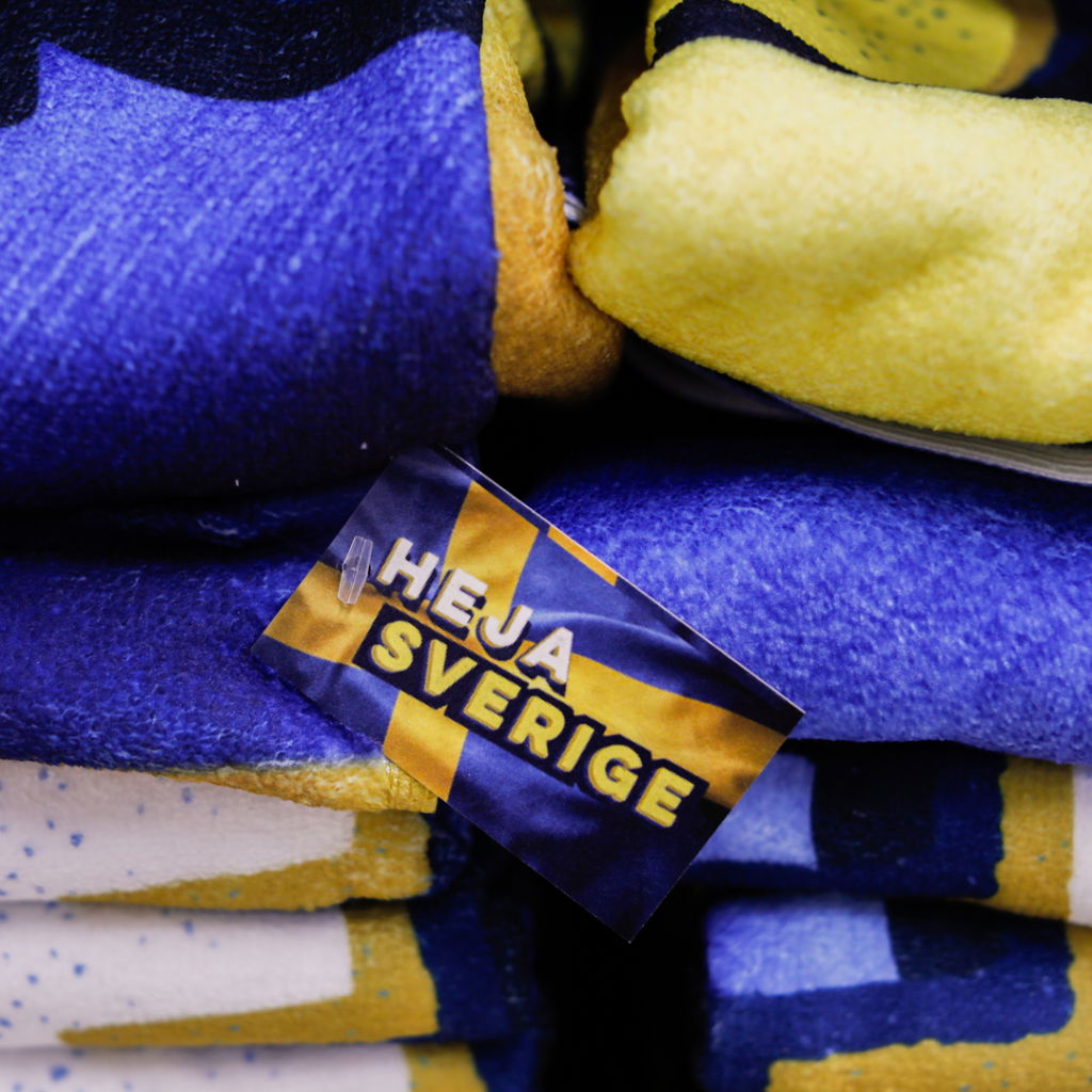 Flera färgglada handdukar i blått och gult med en etikett som säger "Heja Sverige", perfekt för sportevenemang och supporterartiklar.