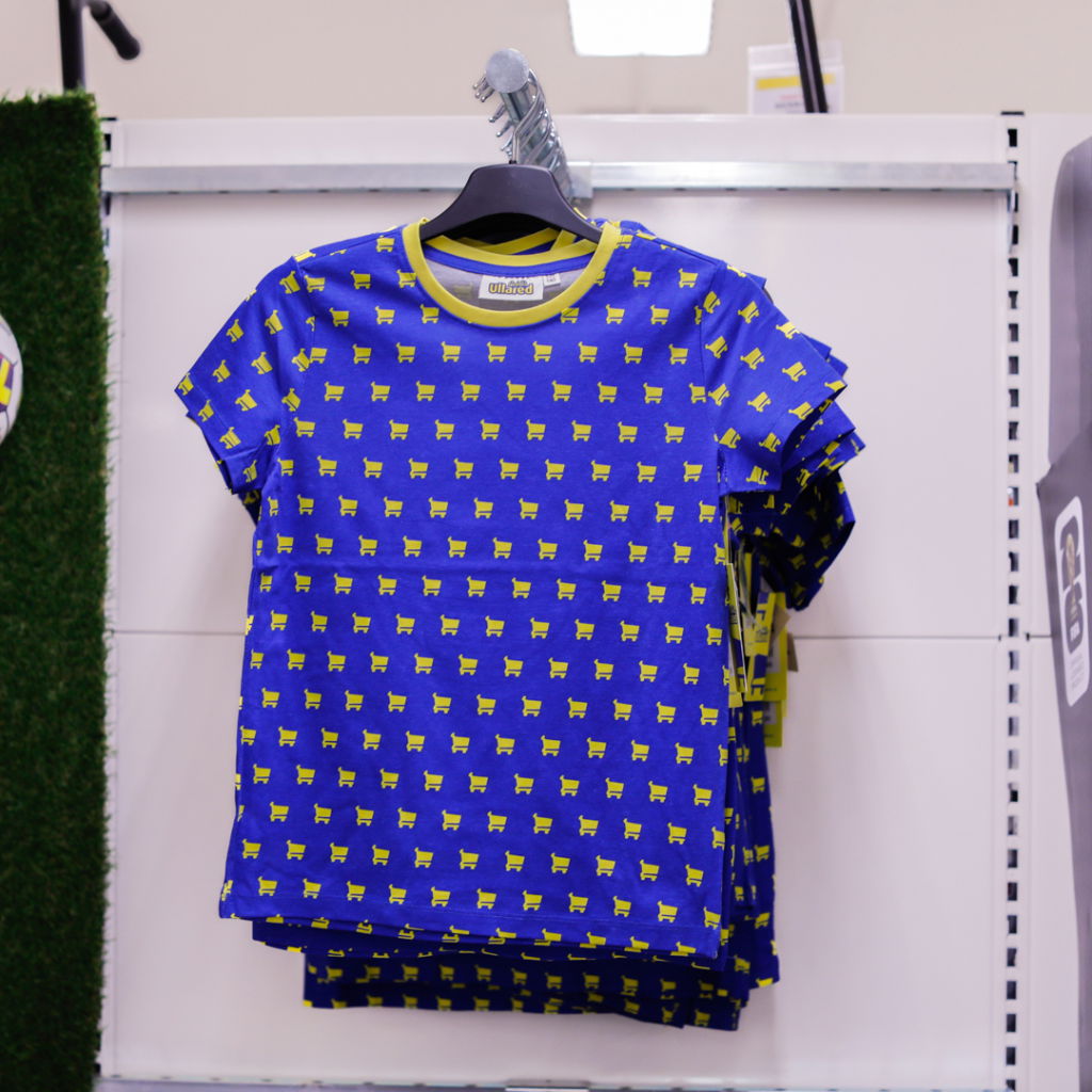Blå t-shirt med grönt mönster av hundar, hängande på klädhängare i butik. Perfekt för djurälskare och barn.