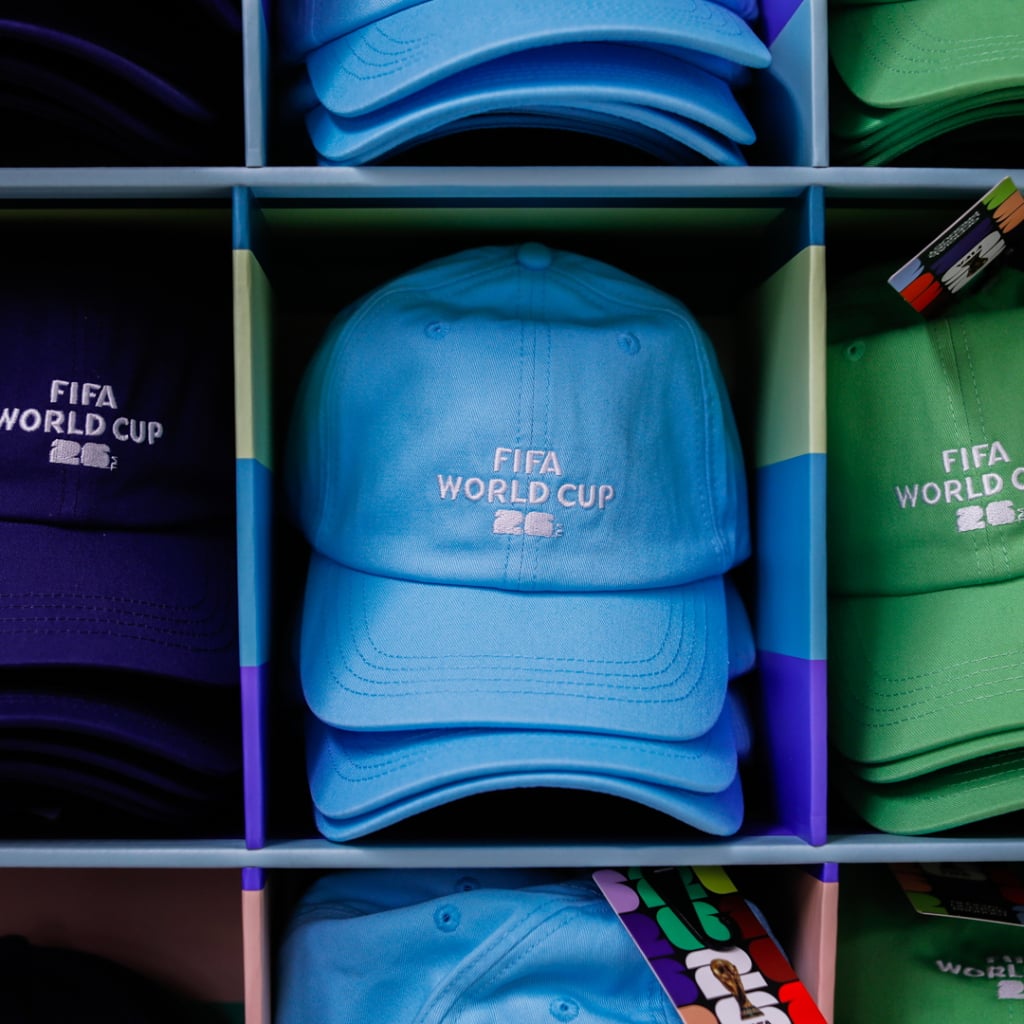 Flera färgglada kepsar med FIFA World Cup-logotypen, inklusive blå, grön och lila, i en hylla.