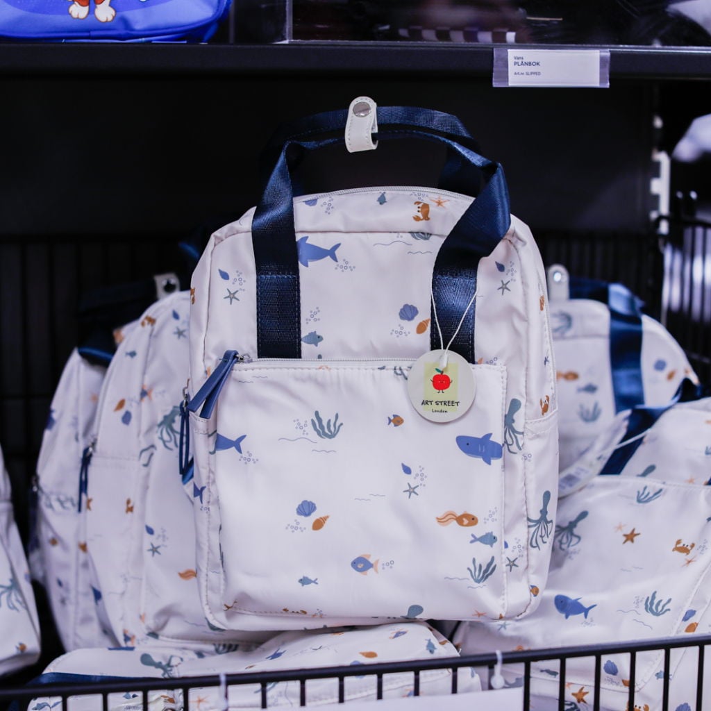 Vadderad ryggsäck med maritimt mönster av fiskar och sjöväxter, perfekt för barn. Säljs i en butik med flera liknande väskor.