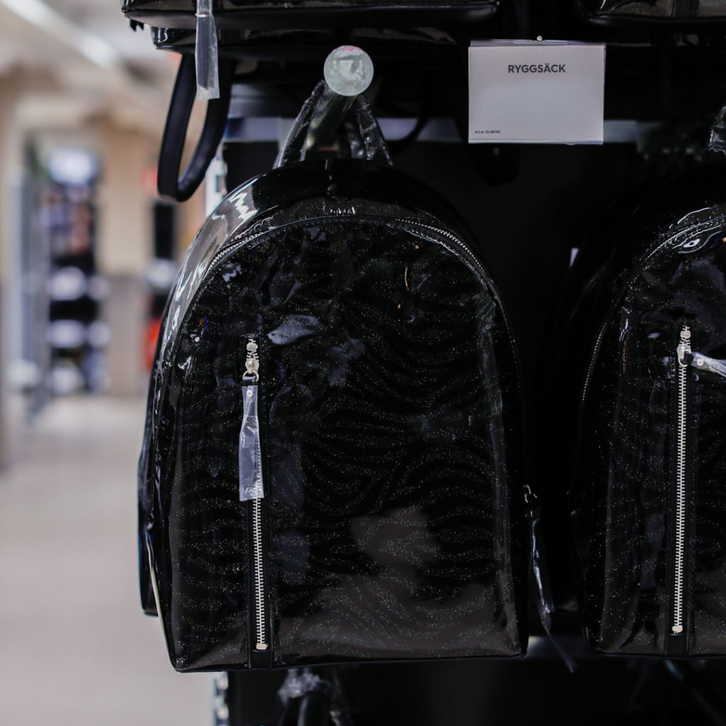 Svart ryggsäck med glittrande mönster, hängande på en butikshylla. Designad för både stil och funktionalitet, perfekt för vardagsbruk eller skola.