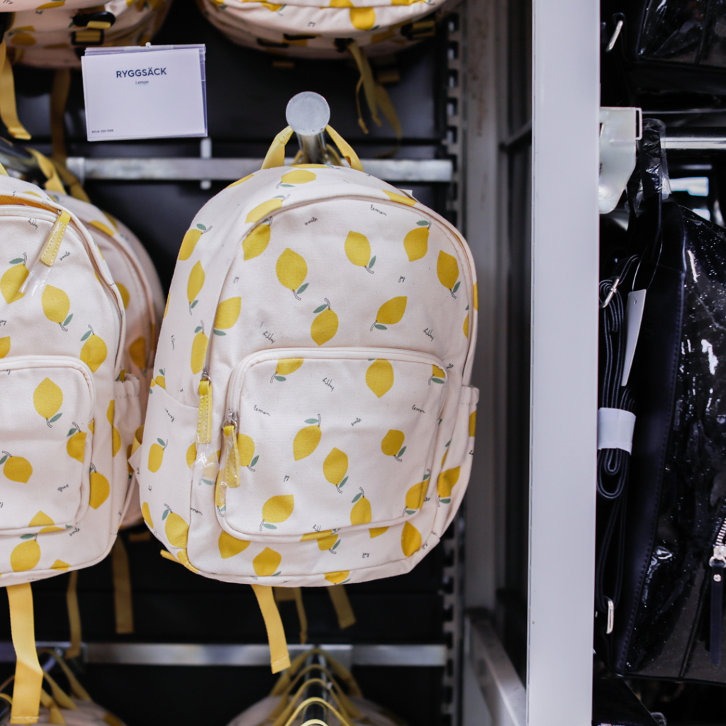 Ryggsäck med citronsmönster, hängande på en hylla i en butik. Designad för både barn och vuxna, perfekt för skola eller fritid.
