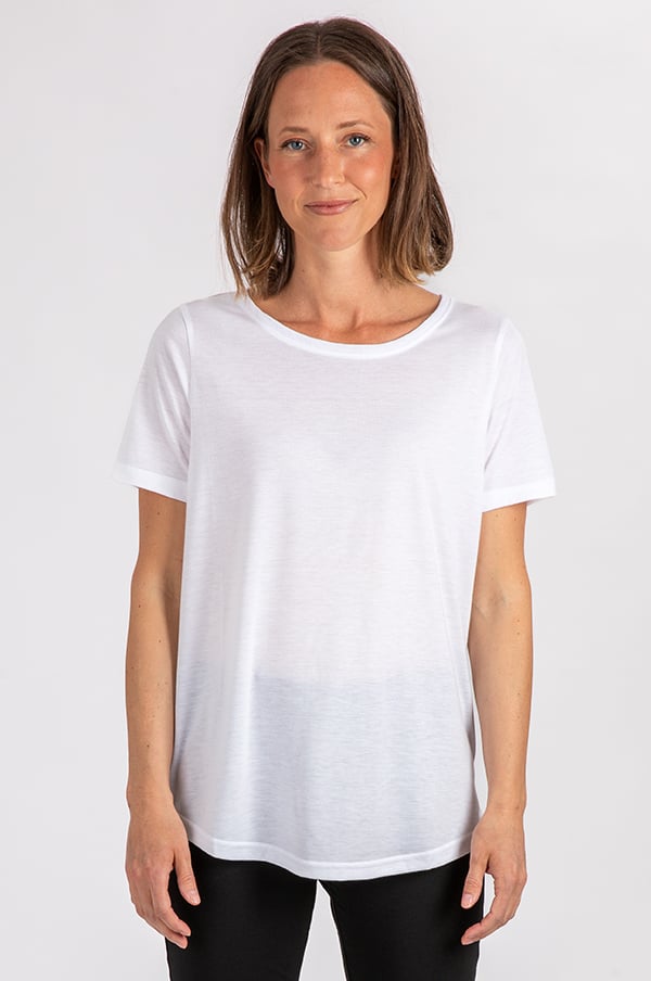 En kvinna i en vit t-shirt med kort ärm, står framför en neutral bakgrund och ler mot kameran. T-shirten har en rund halsringning och är av lätt material, vilket gör den idealisk för både vardagligt bruk och träning.