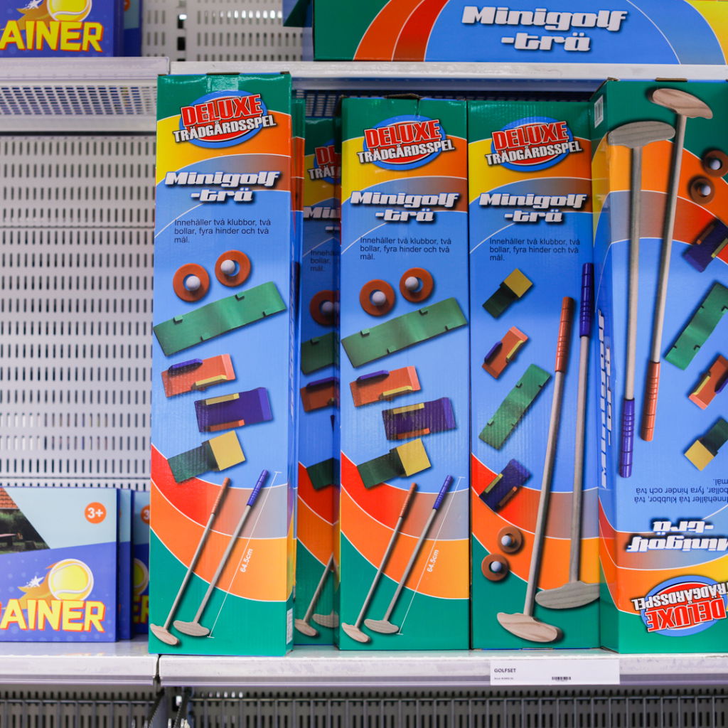Förpackningar med deluxe minigolfspel som innehåller två klubbor, två bollar, fyra hinder och två mål, placerade på en hylla i en leksaksbutik.