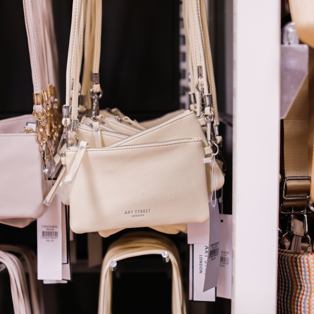 Flera stiliga, ljusa handväskor från varumärket Art Street hänger på en klädhängare i en butik, vilket visar ett urval av moderna accessoarer.