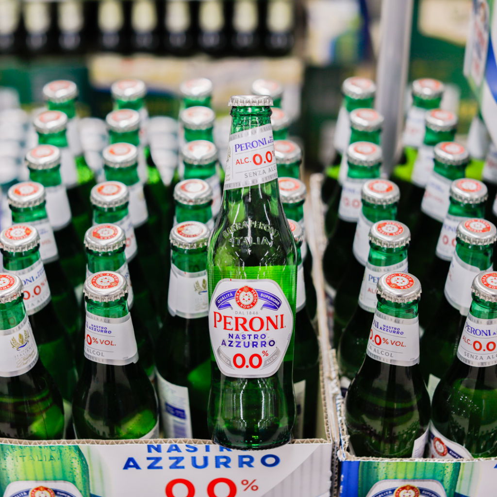 Flaskor av Peroni Nastro Azzurro 0,0% alkoholfri öl i en butik, med fokus på den främre flaskan som tydligt visar etiketten.