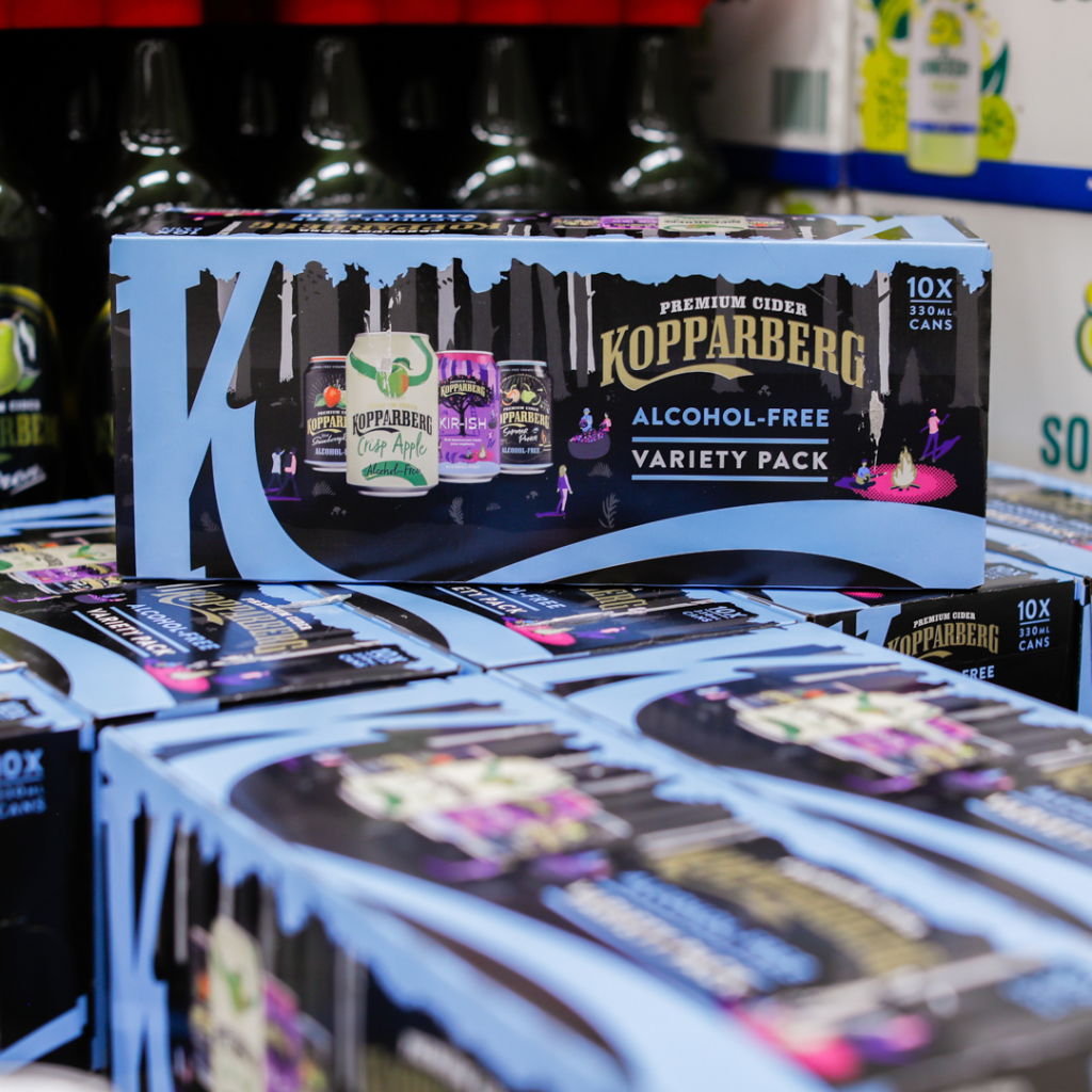 Kopparberg alkoholfritt cider-variety pack med 10 burkar, inklusive smaker som päron och körsbär, placerad på hyllor i en butik.