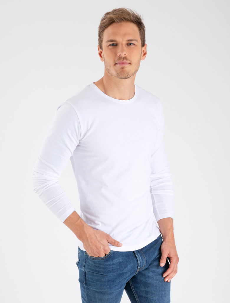 Man i vit långärmad tröja och blå jeans, poserande mot en neutral bakgrund. Tröjan har en enkel design och passar för avslappnade tillfällen.