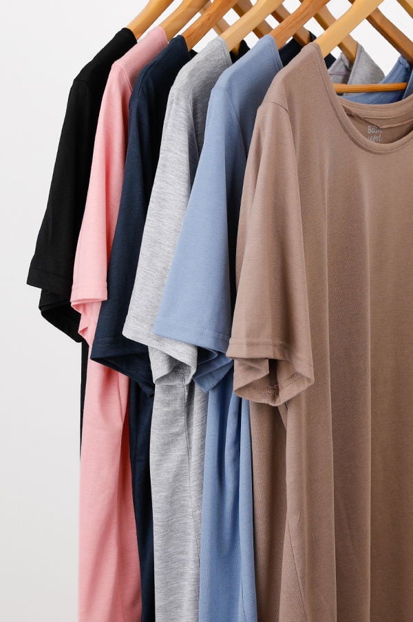 Flera t-shirts i olika färger hängande på en klädhängare, inklusive svart, rosa, grå, blå och brun. T-shirtsen har kort ärm och en avslappnad stil, perfekta för vardagsbruk.
