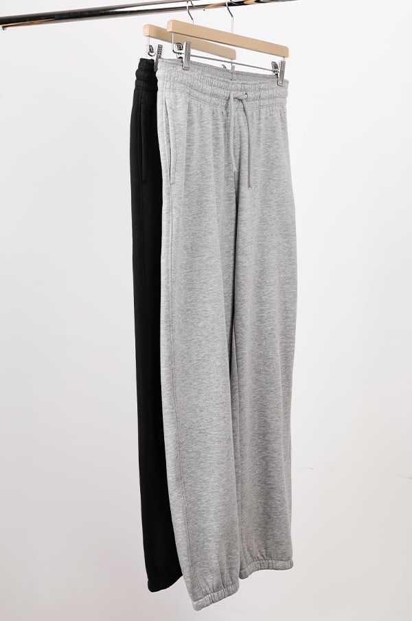 Två par mjukisbyxor hängande på en klädhängare, ett par i grått och ett par i svart, perfekt för avslappnade och sportiga looks.
