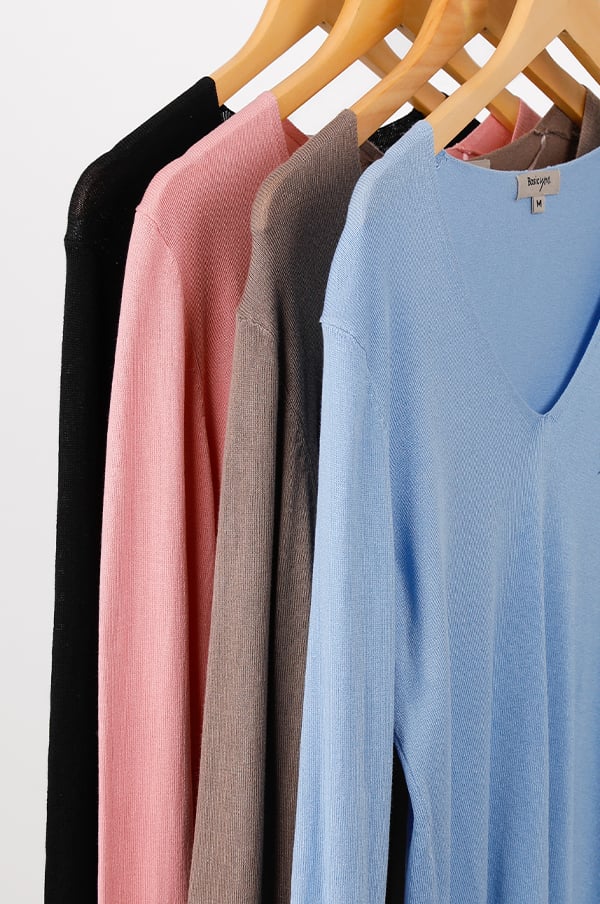 Fyra stickade tröjor i olika färger hängande på klädhängare, inklusive svart, rosa, brun och ljusblå, med en v-ringning. Perfekta för vår- och höstmode.