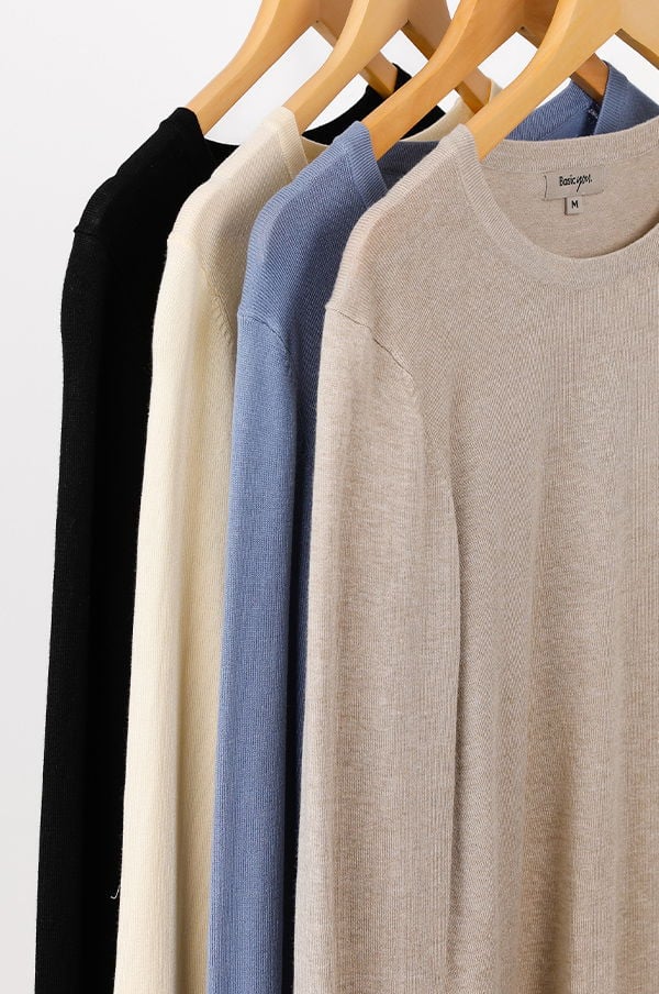 Fyra tröjor i olika färger hänger på klädhängare, inklusive svart, vit, ljusblå och beige. Tröjorna har en enkel design och är i mjukt material, perfekta för både vardag och fest.