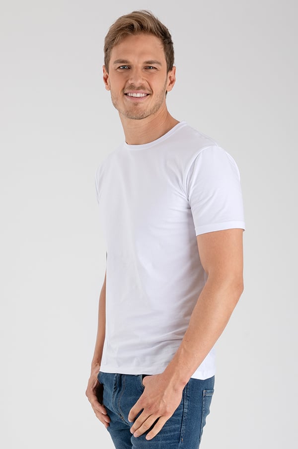 Man i vit t-shirt och blå jeans, poserar med ett leende mot kameran. Bakgrund är neutral och ljus, vilket framhäver klädvalet. Idealisk bild för mode och klädesreklam.