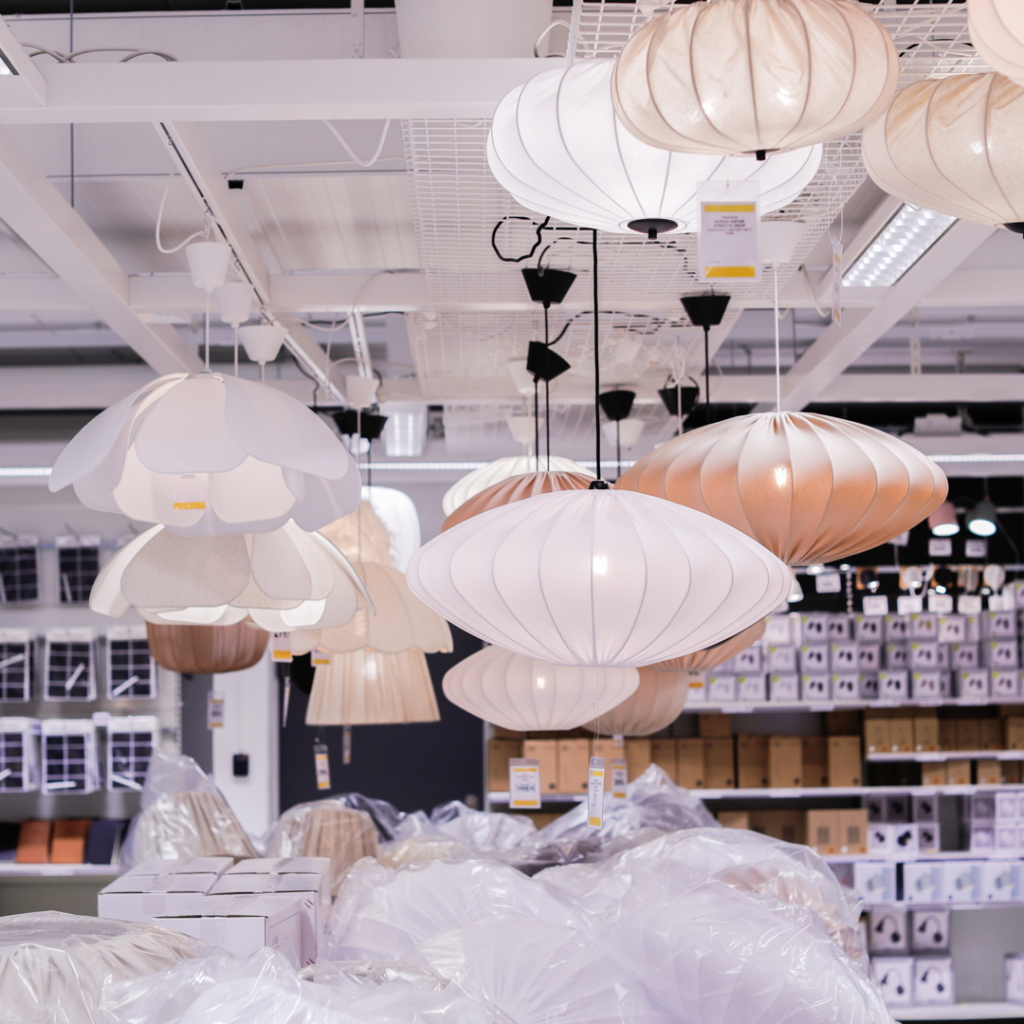 Flera moderna taklampor i olika former och färger hänger från taket i en heminredningsbutik, med förpackningar och plast över golvet.