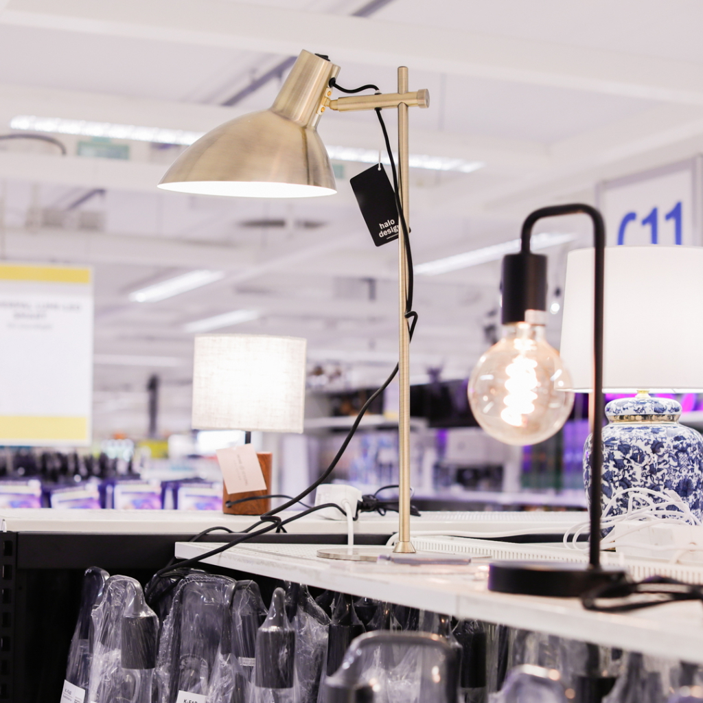 Modern bordsbelysning i en möbelaffär, med en metallisk lampa i fokus, omgiven av olika lampor och en dekorativ blå keramikvas.
