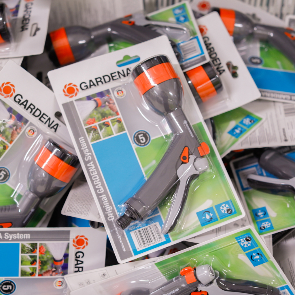 Förpackningar med Gardena sprutpistoler i olika färger, staplade på en yta. Produkten är del av Gardena-systemet och är designad för effektiv bevattning av trädgårdar.