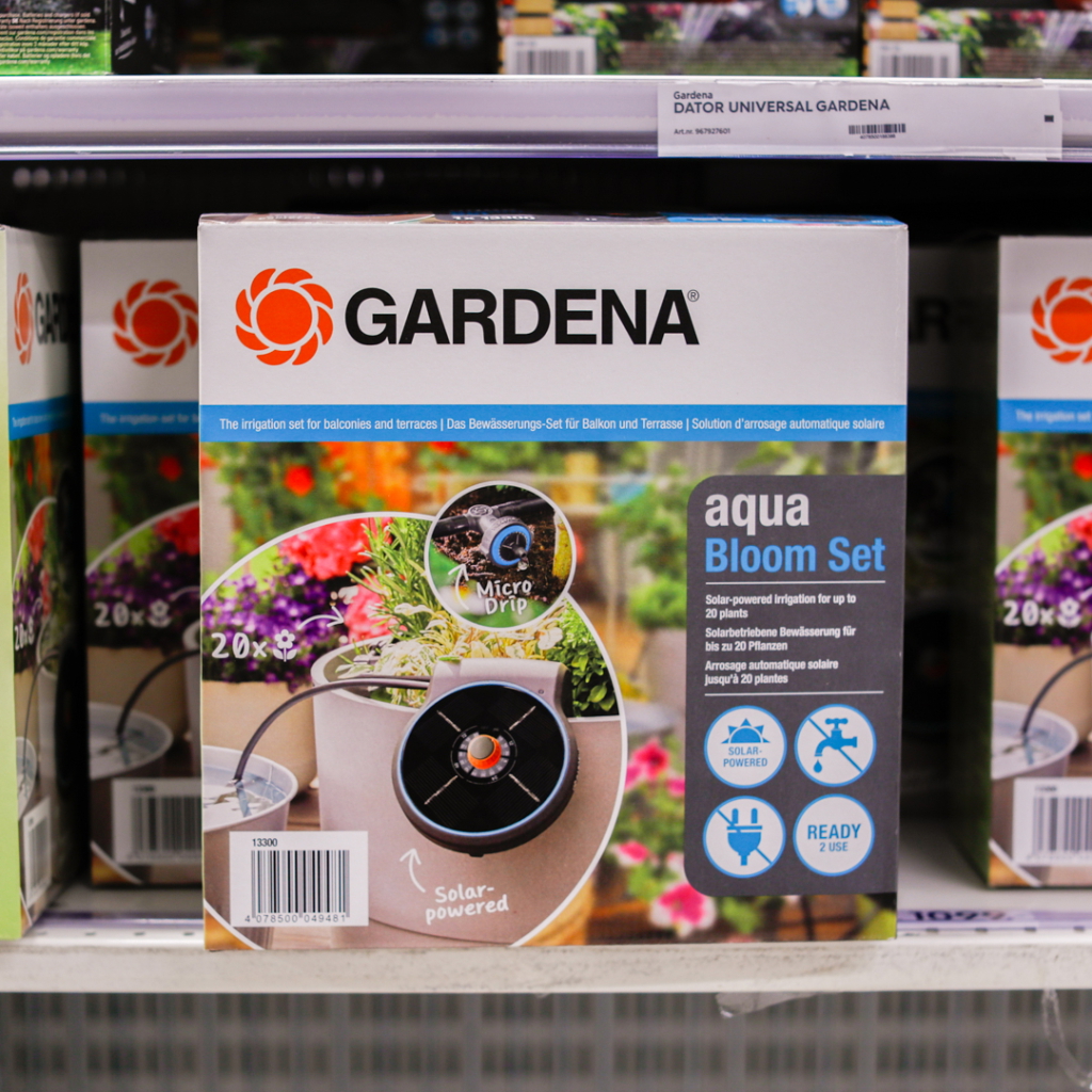 Förpackning av Gardena aqua Bloom Set, ett solenergidrivet bevattningssystem för balkonger och terrasser, som kan vattna upp till 20 växter. Produkten innehåller Micro Drip-teknik och är redo att användas.