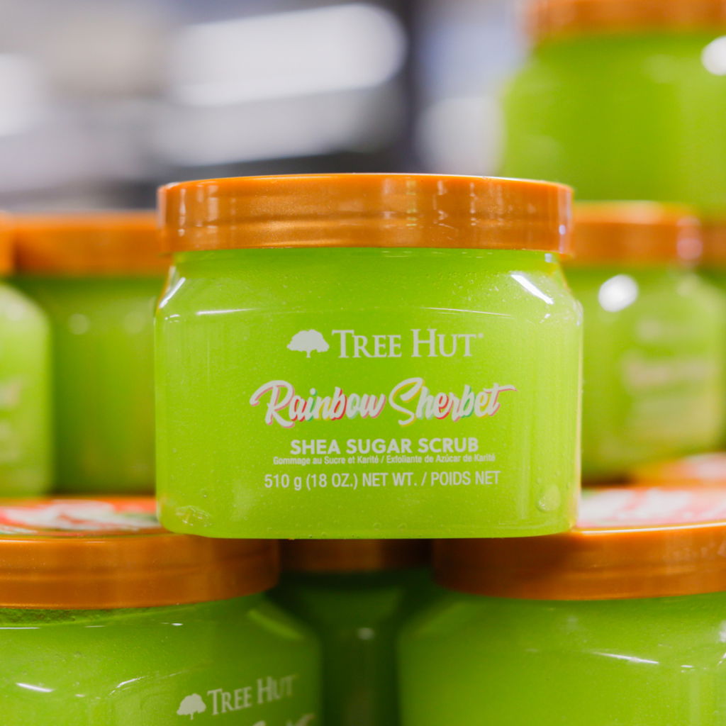 Grön burk med Tree Hut Rainbow Sherbet shea sugar scrub, 510 g, placerad bland andra burkar. Produkten är en kroppsskrubb som exfolierar och återfuktar huden.