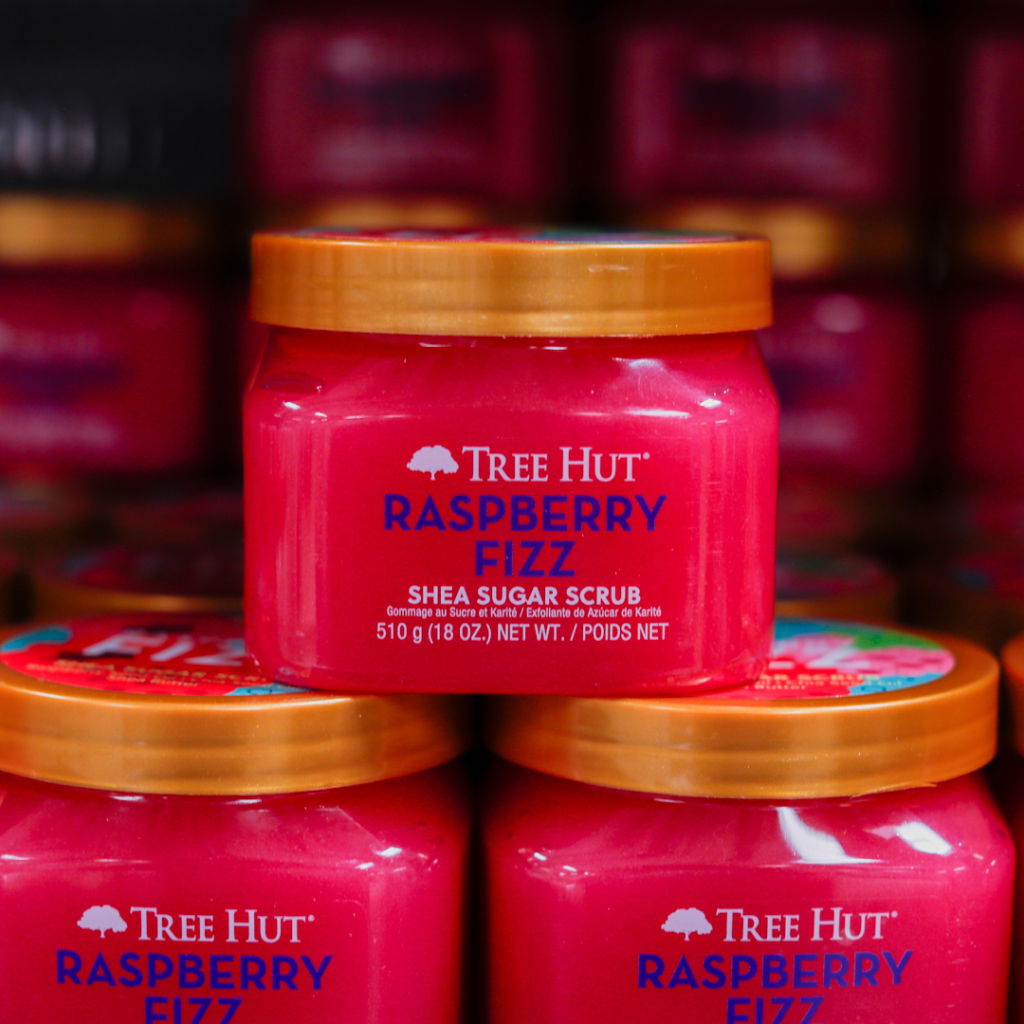 Rosa burk med Tree Hut Raspberry Fizz sheasmörsskrubb, 510 g, placerad bland andra liknande produkter i hyllan.