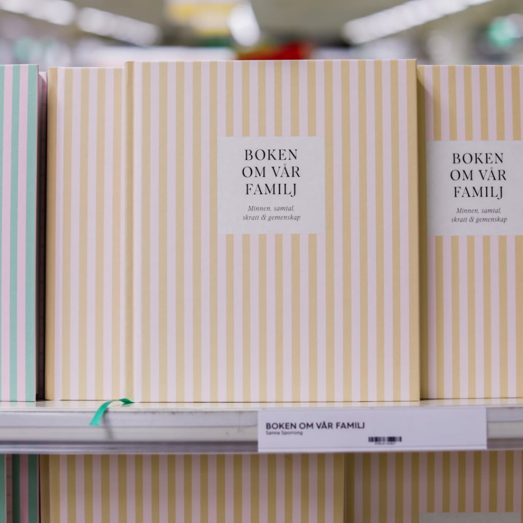 Böcker med titeln "Boken om vår familj" på en hylla, med fokus på minnen, samtal, skratt och gemenskap.