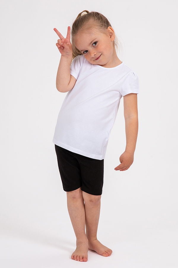 Litet barn i vit t-shirt och svarta shorts poserar med ett fredstecken. Barnet har långt hår och står barfota på en vit bakgrund.