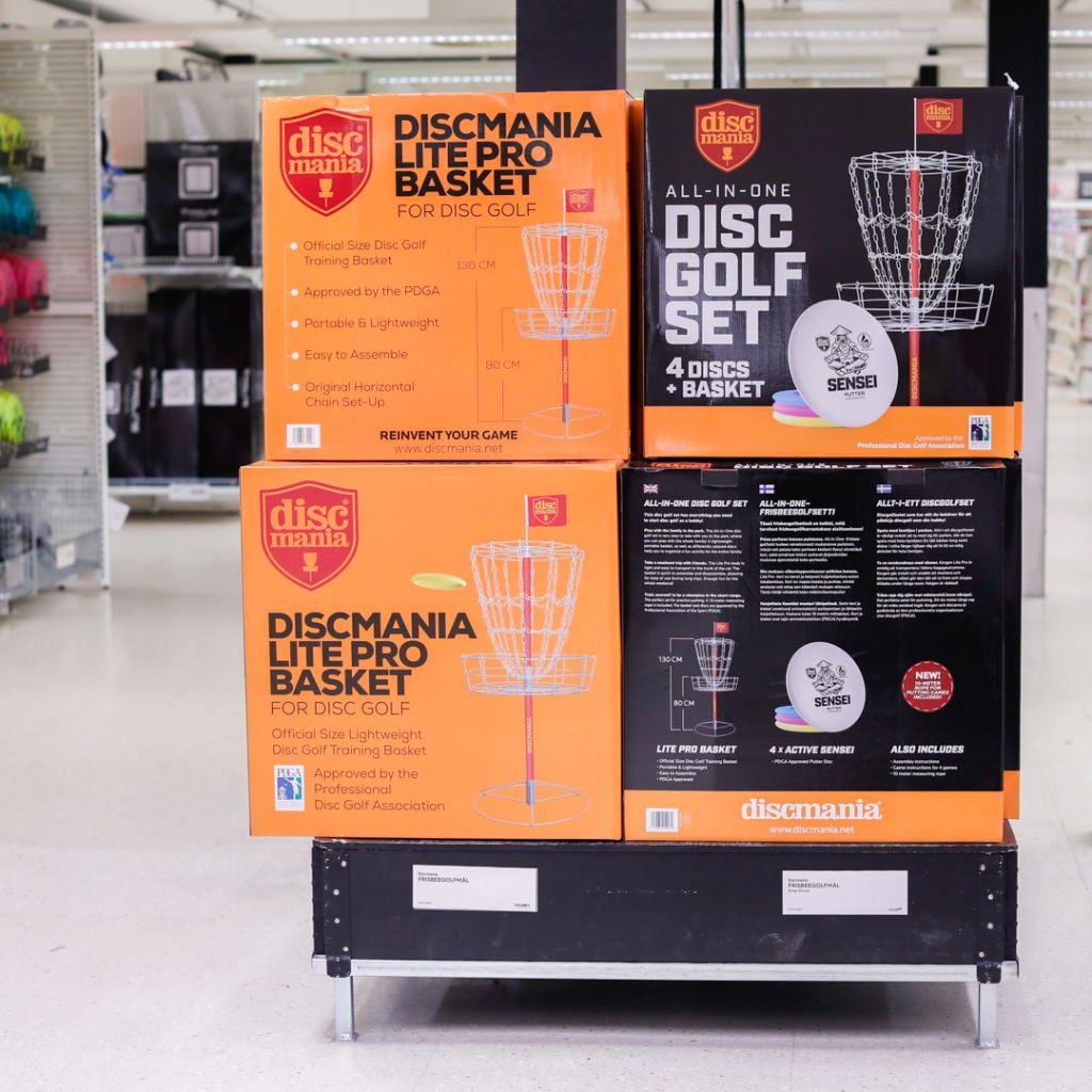 Bild på Discmania-produkter för discgolf, inklusive Discmania Lite Pro Basket och ett allt-i-ett discgolf-set med fyra diskar och korg. Korgarna är godkända av PDGA och designade för enkel montering och portabilitet.