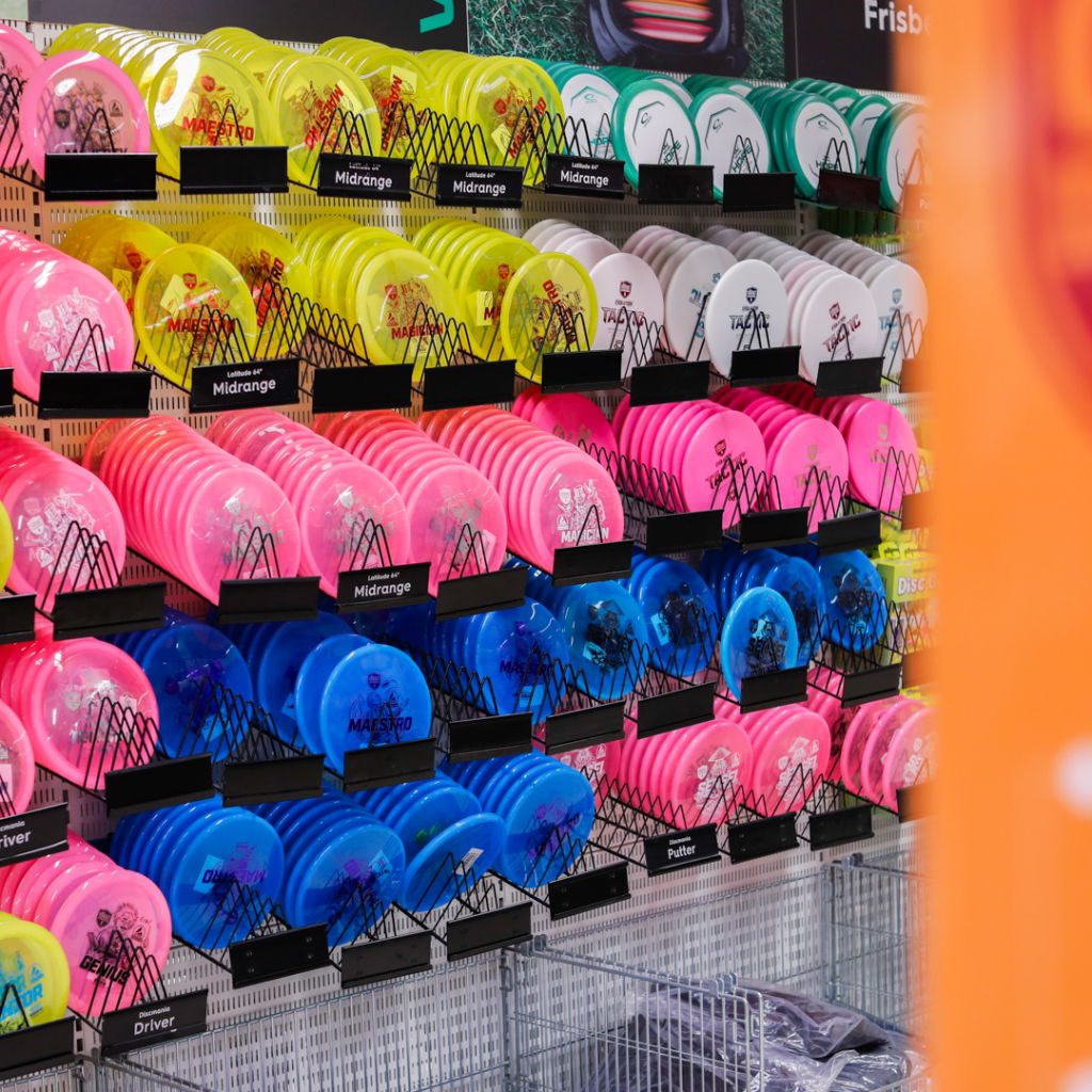 Färgglada frisbees i olika kategorier som midrange, driver och putter, organiserade på hyllor i en sportbutik.