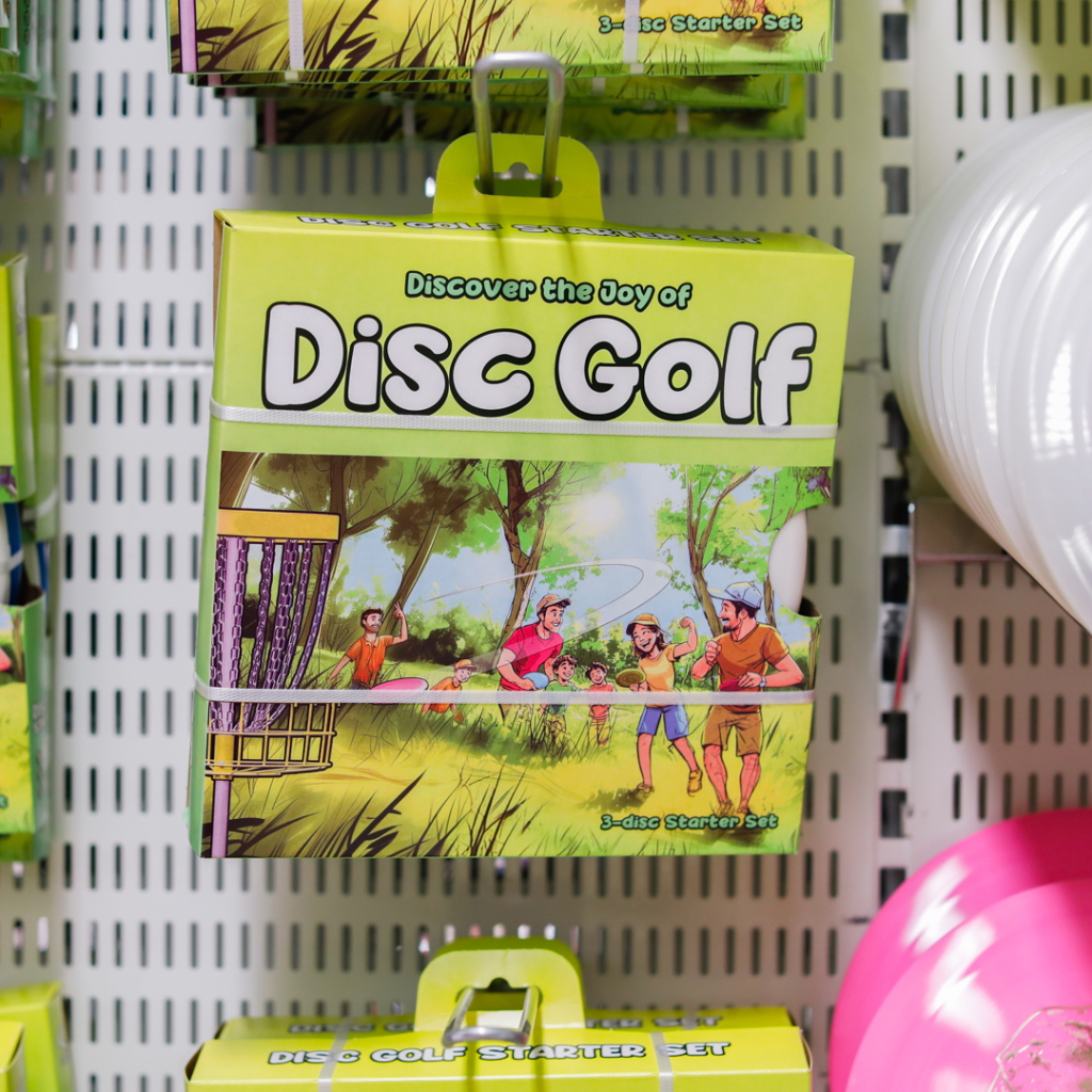 Förpackning för Disc Golf startkit med tre discar, illustrerad med glada människor som spelar disc golf i en grönskande park.