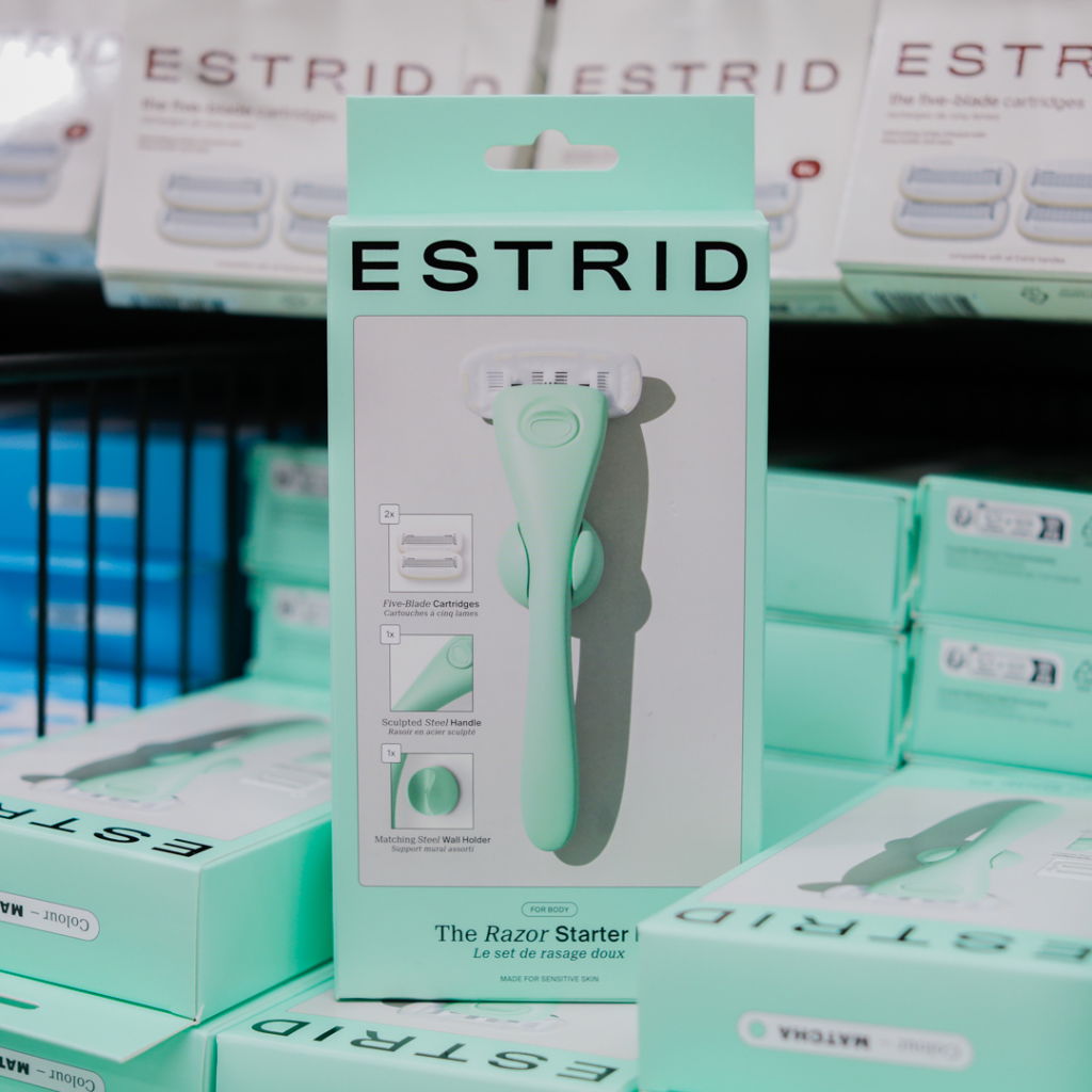 Förpackning av Estrid rakapparat med fembladiga rakblad, designad för känslig hud. Innehåller en skulpterad handtag och en matchande vägghållare.