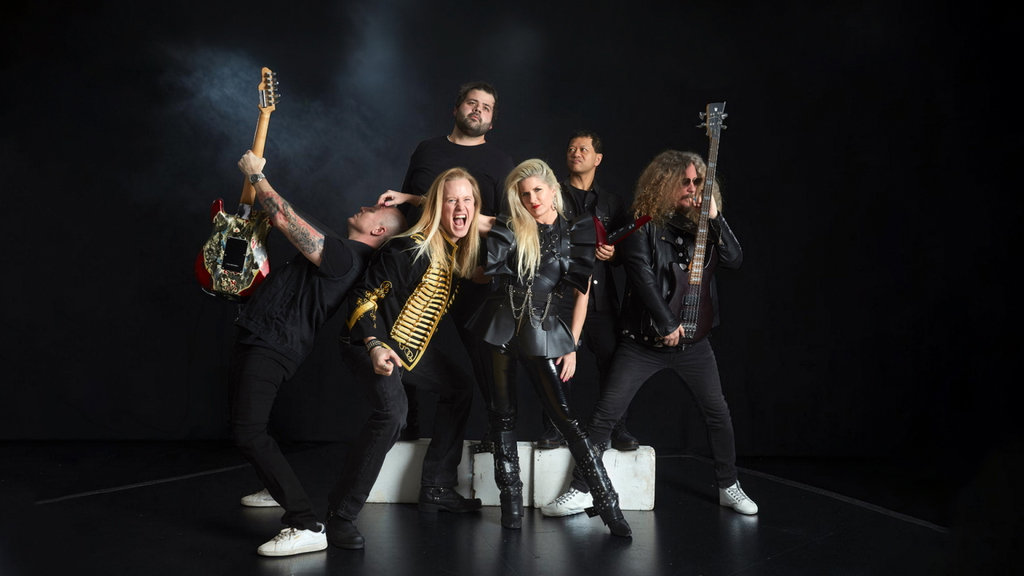 Bild av ett rockband som poserar på scen med gitarrer och bas. Bandmedlemmarna visar en energisk och dynamisk attityd, klädda i svarta läderkläder och med olika instrument. Bakgrunden är mörk för att framhäva bandets närvaro och stil.