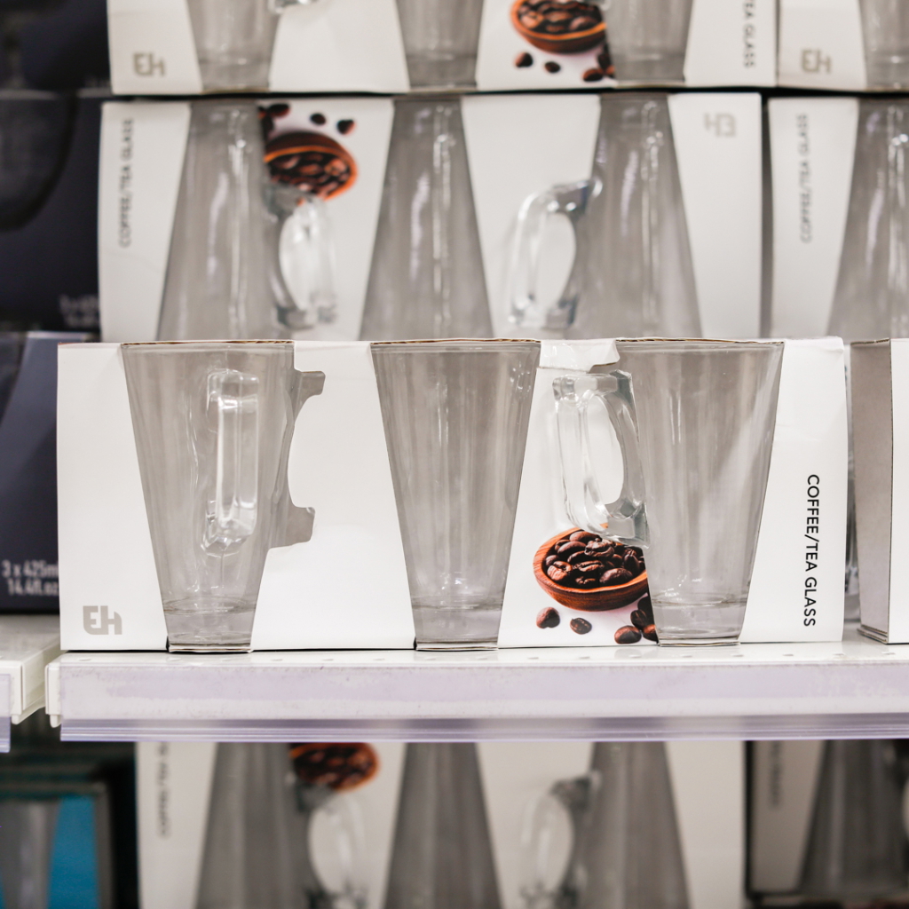 Set med glas för kaffe och te, placerade på en hylla i en butik. Glasen har en modern design och är förpackade i en låda med bilder av kaffebönor.