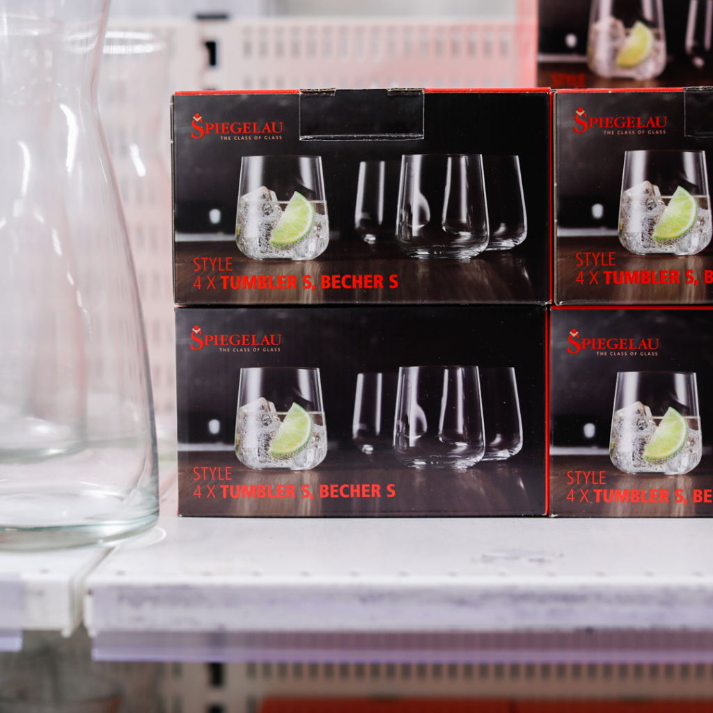 Förpackning med fyra Spiegelau tumblerglas i stilfull design, placerad på en hylla i en butik. I förgrunden syns en glasbehållare.
