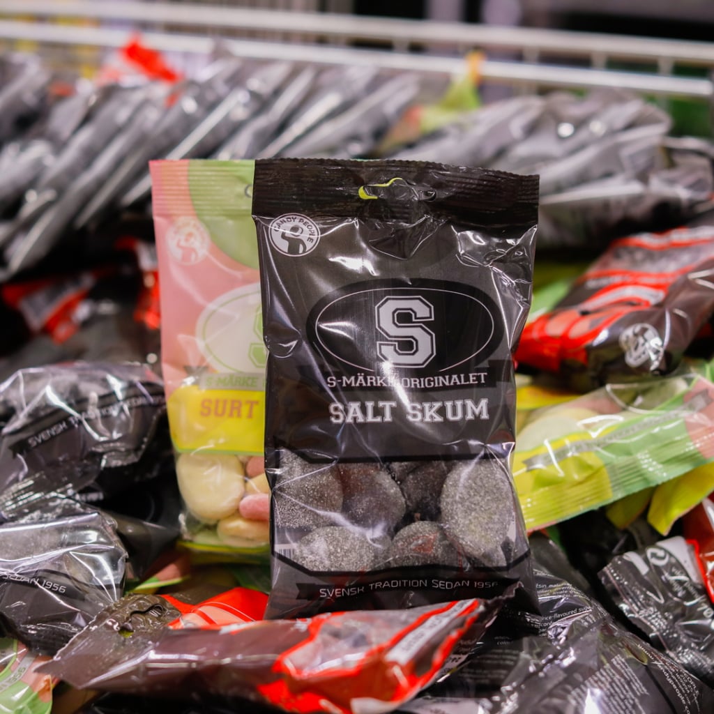 Förpackning av salt skumgodis från S-märket, omgiven av olika godispåsar i en butik, som visar den svenska godistraditionen.