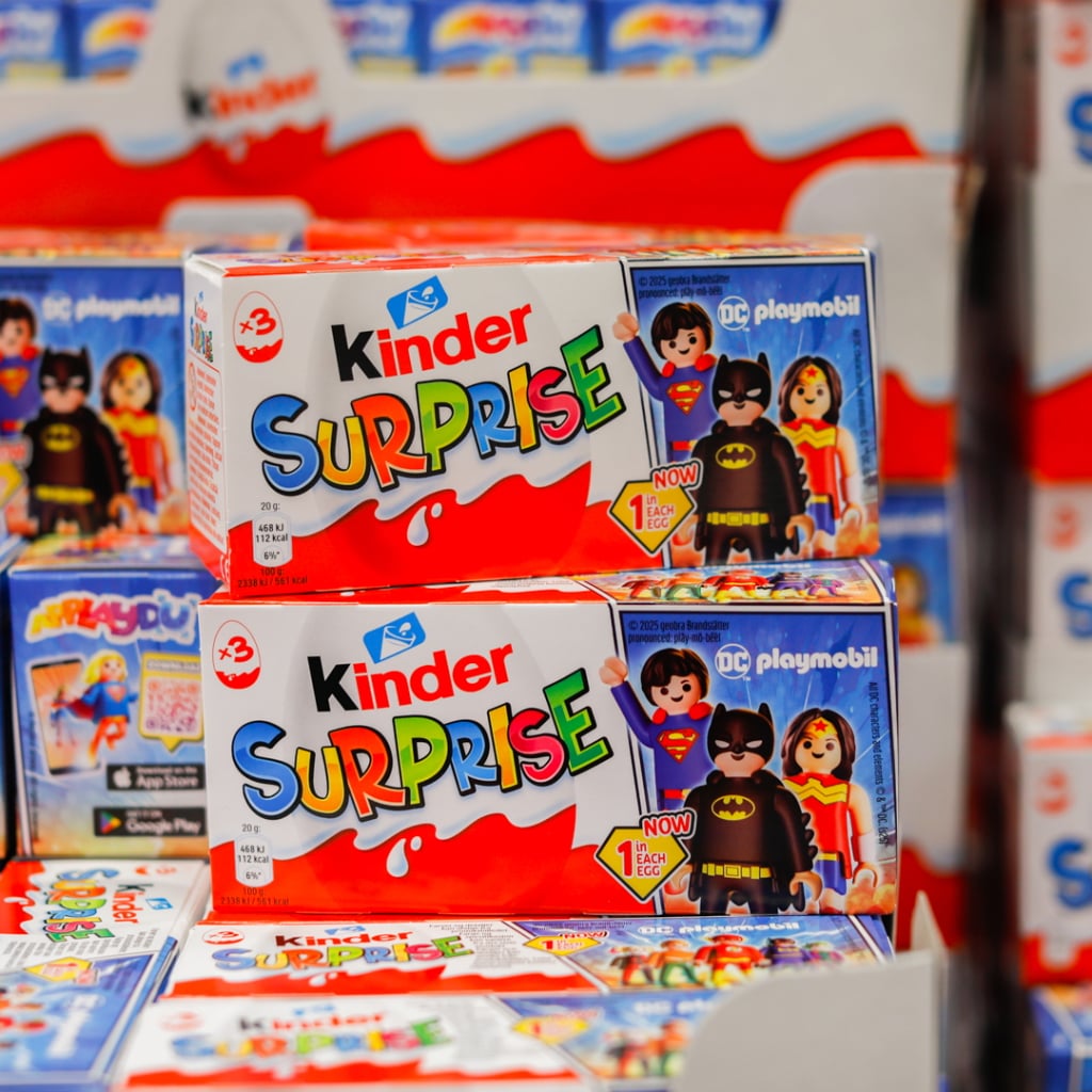 Förpackningar av Kinder Surprise med DC Playmobil-figurer, inklusive Superman och Batman, i en färgglad butiksmiljö.