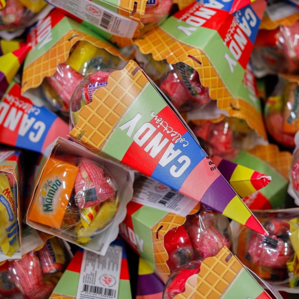 Färgglada godiskonfekter i pappersförpackningar, staplade i en hög, med varumärket "Candy" synligt på flera förpackningar.