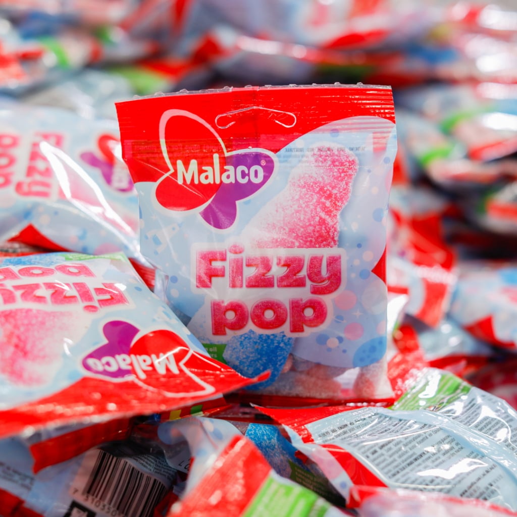 Förpackningar av Malacos godis "Fizzy Pop" i en färgglad och sprudlande miljö, med fokus på den tydliga märkningen och designen.
