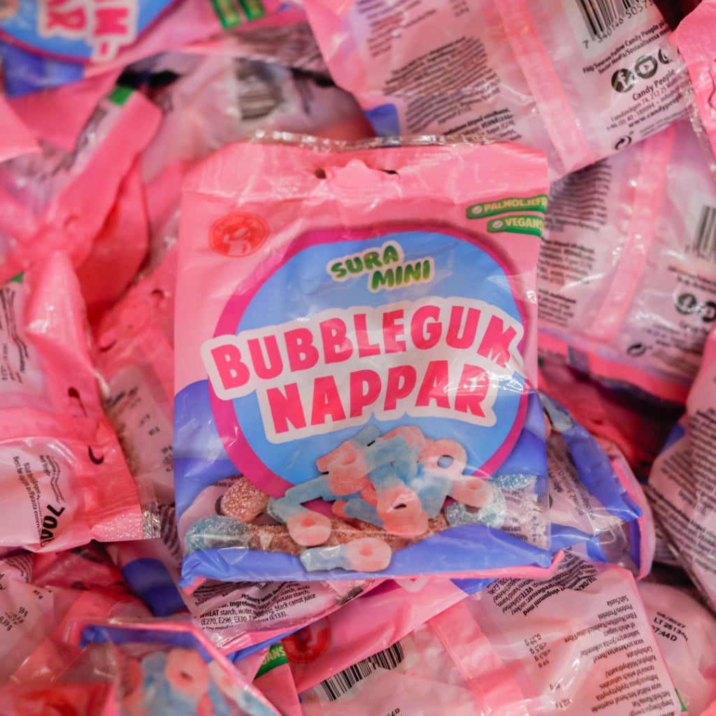 Förpackning med sura mini bubblegum nappar, en färgglad godisprodukt, omgiven av flera liknande påsar.