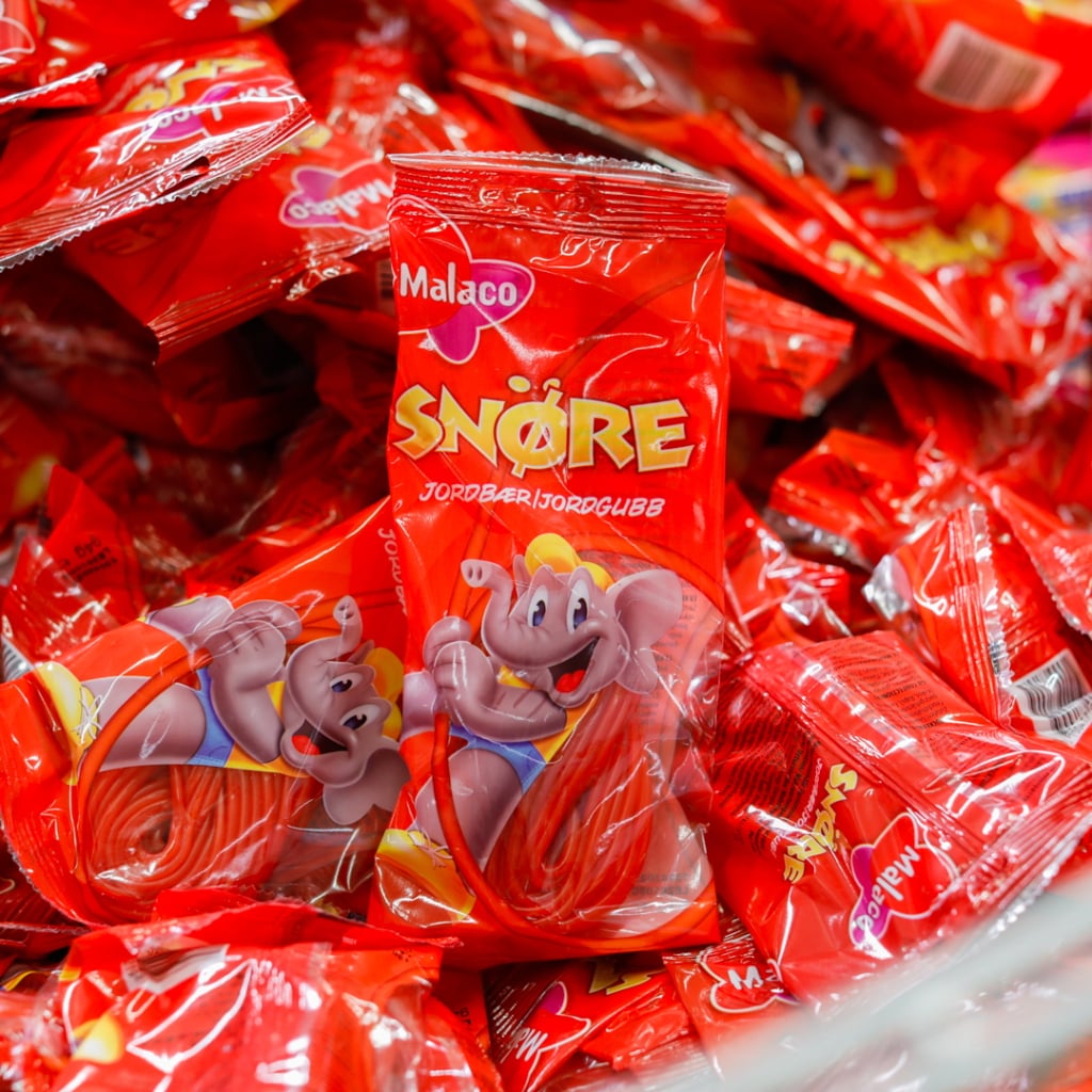 Förpackning av Malacos Snöre godis med jordgubbssmak, omgiven av flera andra förpackningar med samma produkt.