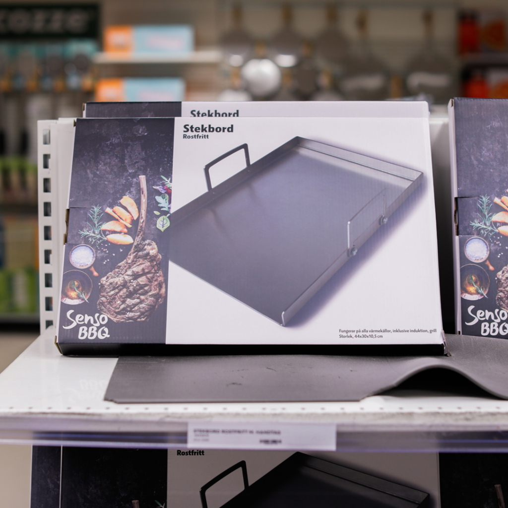 Alt-text: Stekbord från Senso BBQ i rostfritt stål, designat för grill och induktion, med måtten 44x30x5 cm, placerat på en hylla i en butik.