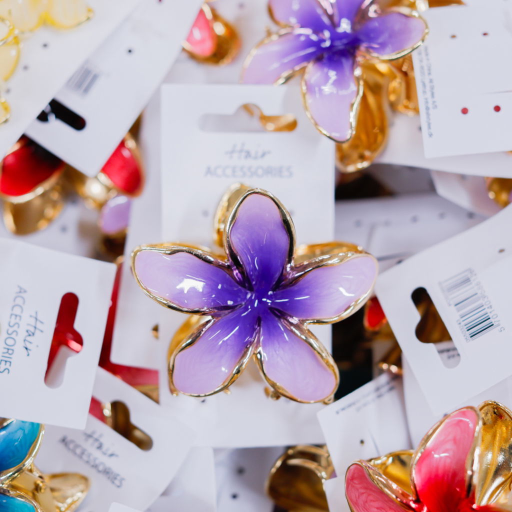 Färgglada håraccessoarer i form av blommor, inklusive lila, rosa och blå, förpackade på kort med etiketten "Hair Accessories". Perfekta för att ge en stilfull touch till frisyrer.